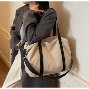 Detail of canvas tote bag showing black leather straps and side metal buckle design
