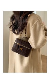 Detail of dark brown quilted crossbody bag with metal chain strap on beige coat