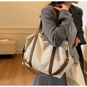 Detail of large canvas tote bag with brown leather handles and wide shoulder strap