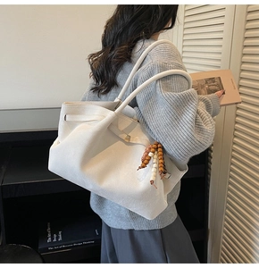 Detail of white suede tote bag featuring bohemian wooden bead charm and slim shoulder straps