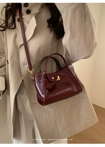Detail of dark red vintage leather handbag with gold buckle on a beige trench coat