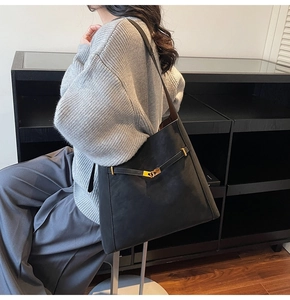 Detail of matte black bucket bag with gold clasp and leather strap on grey sweater