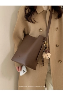 Detail of dark brown leather bucket bag with plush bear charm and pebbled texture