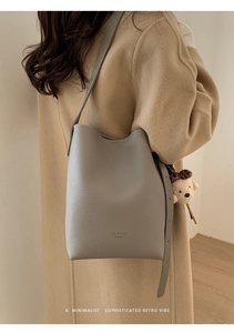 Gray pebble leather bucket bag with bear charm and adjustable strap shown on model