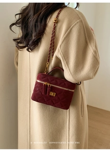 Model wearing a burgundy velvet quilted vanity bag with gold chain and top handle