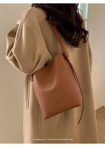 Close-up of a brown leather bucket bag featuring pebbled texture and gold buckle detail
