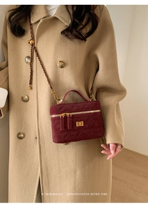 Detail of burgundy velvet crossbody bag with gold chain strap on beige wool coat