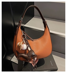 Detail der orangefarbenen Hobo-Tasche aus Leder mit Dackel-Anhänger auf schwarzen Büchern