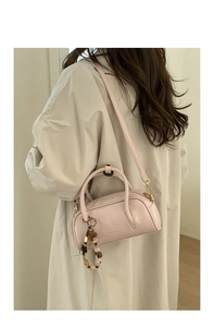 Detail of light pink baguette bag with beaded charm on a beige trench coat
