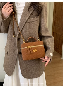 Detail of a brown quilted crossbody bag featuring a golden chain strap and twist lock design