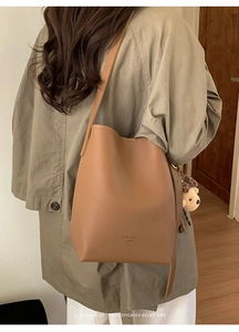 Detail of camel leather bucket bag with litchi grain and a cute plush bear pendant