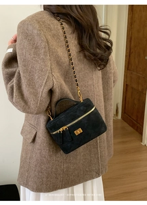 Detail of black suede mini crossbody bag featuring a golden twist lock and chain strap