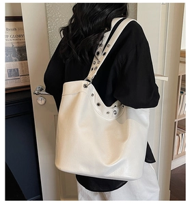Detail of white leather tote bag with silver metal eyelets on shoulder straps and edges