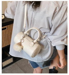 Detailed view of a white cylindrical Boston bag with a cute plush lamb pendant and leather strap