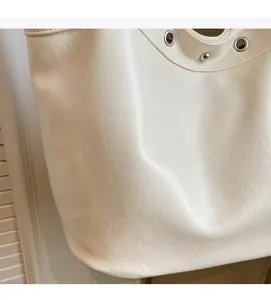 Detail of soft white PU leather texture with silver metal eyelets on a tote bag