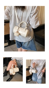 Detail of white cylindrical Boston bag with plush charm and versatile carrying options