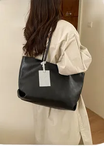 Detail view of large black tote bag with white cartoon dog tag and soft leather texture