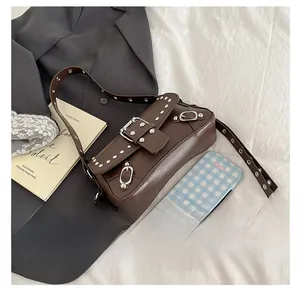 Detail of dark brown leather shoulder bag with silver buckles and studs on white cloth