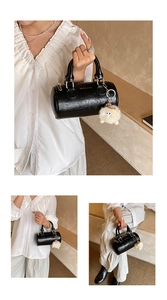 Detail of black cylindrical pillow bag in glossy cracked leather with plush toy charm