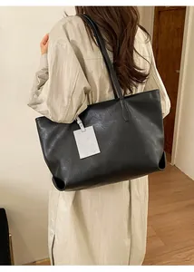 Detailed view of the black leather tote bag featuring rich texture and a white cartoon tag
