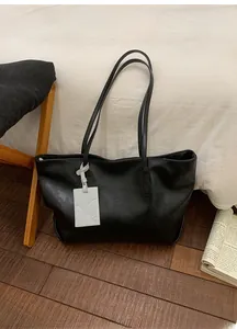 Close-up of black leather tote bag featuring a minimalist gray card holder charm