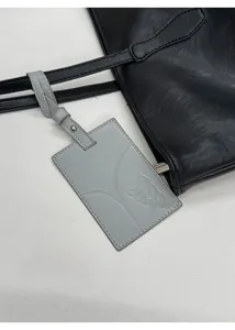 Detail of a gray rectangle luggage tag with embossed bulldog motif on a black leather tote