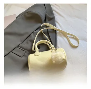 Detail of cream barrel crossbody bag with grainy leather texture and plush pompom charm