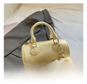 Close-up of beige leather cylinder bag with fashion lettering and cute plush charm