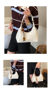 Detail of white half-moon underarm bag with wooden beads tassel and golden logo lettering