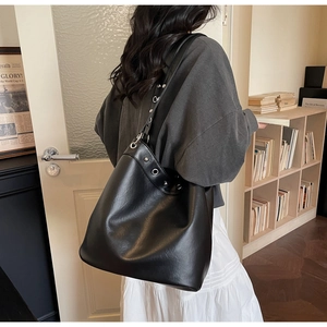 Detail of black leather tote bag with silver metal eyelets shown on a shoulder
