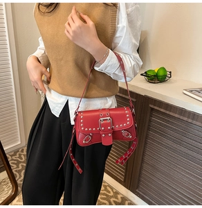 Close-up of red leather shoulder bag featuring silver rivets and metal buckle closure