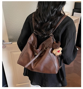 Detail of dark brown leather tote bag with a cute bear pendant worn as a backpack