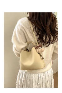 Chic cream bucket bag with plush bear charm worn over a white knit outfit for spring