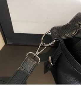 Close-up of shiny silver lobster clasp and D-ring on a black textured leather tote bag