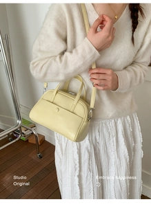 Detail of cream Boston handbag with top handles and cross-body strap on a model