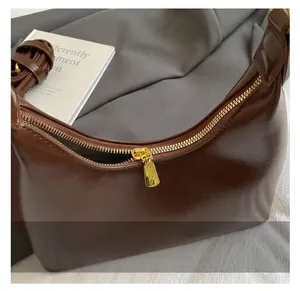 Detailed close-up of smooth brown patent leather bag with premium gold zipper and engraving
