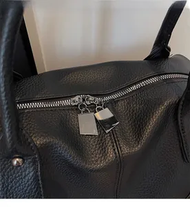 Close-up of smooth dual zippers on black litchi pattern leather tote bag with silver hardware