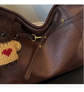 Detailed shot of dark brown pebbled leather bag with gold hardware and bear charm