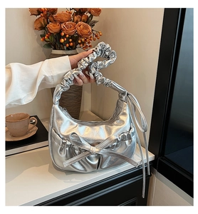 Close-up of a metallic silver pleated handbag with a large bow and decorative long ribbons