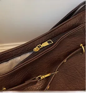 Close-up of smooth gold zipper and textured litchi grain leather on dark brown tote bag