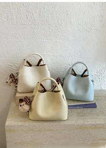 Three minimalist bucket bags in beige, yellow and blue with cute bear charms on a stone surface