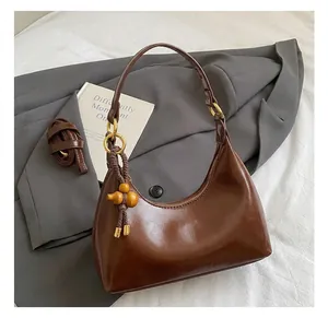 Detail of dark brown leather hobo bag with gold metal rings and wooden gourd pendant