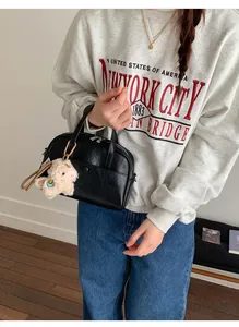 Detail of a minimalist black bucket bag with a cute white plush charm and silver hardware