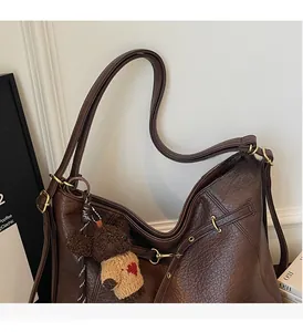 Detail view of brown leather tote bag with sturdy handles and cute teddy bear pendant