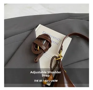 Detail view of deep brown leather bag strap with gold buckle and beaded charm accessory