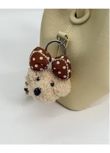 Detail of cute beige curly plush puppy bag charm with brown bow on leather bucket bag