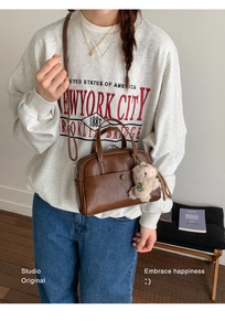 Detail of a brown leather Boston bag featuring a front pocket and a cute bear charm