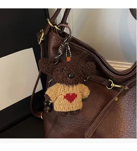 Detail of a brown lychee pattern bucket bag with a plush bear charm in heart sweater