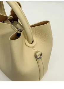 Detailed view of cream leather bucket bag showing litchi grain texture and thick handle