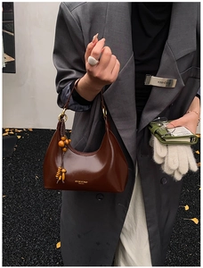 Detalle de bolso hobo marrón oscuro con borla de cuentas de madera y acabado en charol brillante